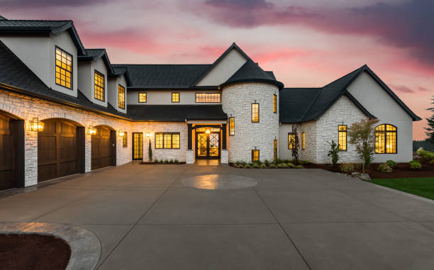 Stunning luxury home exterior at sunset new luxury home with three car garage, large driveway and glowing exterior and interior lights rich lifestyle stock pictures, royalty-free photos & images