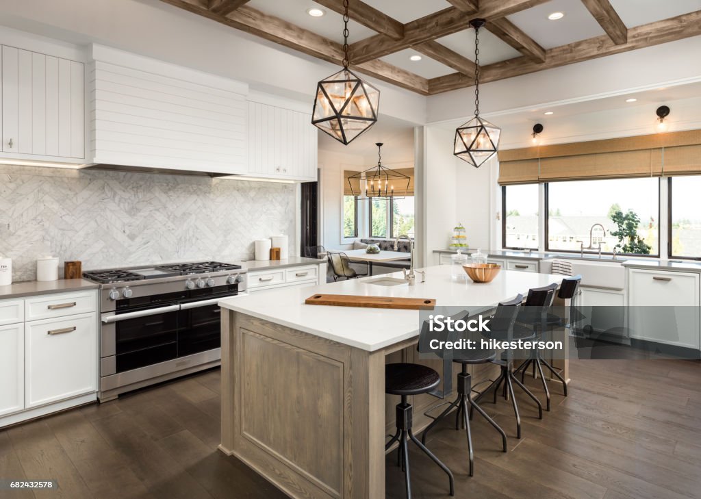 beautiful kitchen in new luxury home with island and pendant light fixtures Kitchen Interior with Island, Sink, Cabinets, and Hardwood Floors in New Luxury Home. Includes elegant pendant light fixtures and wood beam ceiling Kitchen Stock Photo