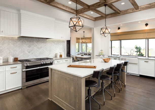 beautiful kitchen in new luxury home with island and pendant light fixtures Kitchen Interior with Island, Sink, Cabinets, and Hardwood Floors in New Luxury Home. Includes elegant pendant light fixtures and wood beam ceiling stainless steel photos stock pictures, royalty-free photos & images