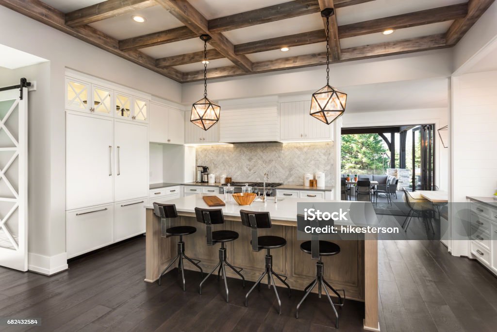 beautiful kitchen in new luxury home with island and pendant light fixtures Kitchen Interior with Island, Sink, Cabinets, and Hardwood Floors in New Luxury Home. Includes elegant pendant light fixtures and wood beam ceiling Luxury Stock Photo