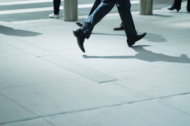 Close-up of dress shoes and fashionable suit as businessman runs past other pedestrians on modern city sidewalk