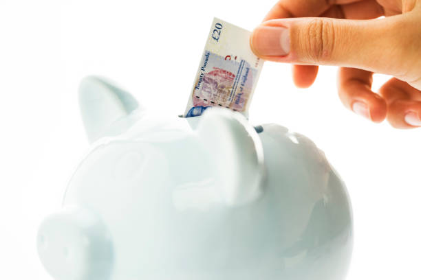 Hand putting small size British pound paper banknotes in piggy bank