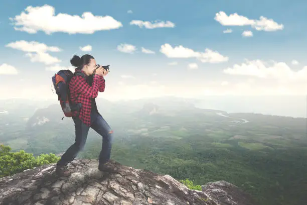 Image of young male standing on the mountain while taking a photo of amazing landscapes
