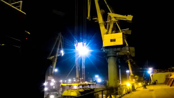 Industrial seaport at night. The rotation of the car with grain using a tower crane.