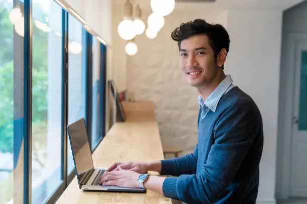 Photo of Portrait of a young adult male sat using his laptop in a modern office