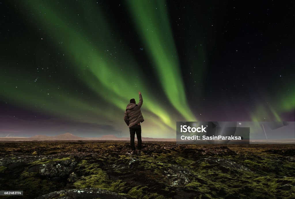 landscape of amazing beautiful  natural phenomenon Aurora Borealis, with a man raising arm , traveling in Iceland Aurora Borealis Stock Photo