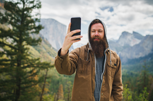cool bearded man taking selfie photo with smartphone infront of yosemite