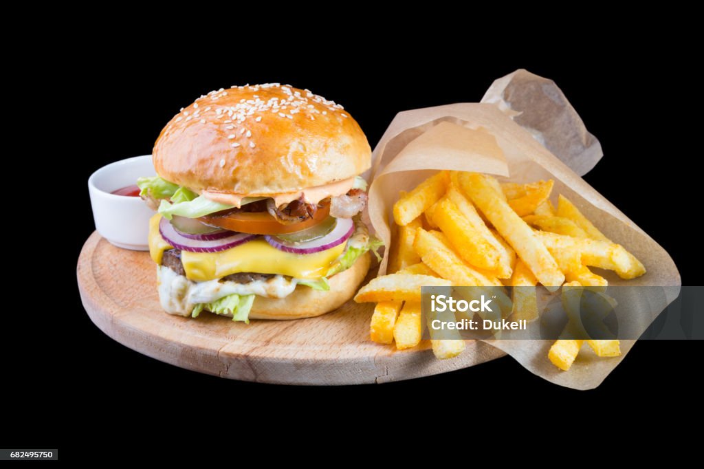 Burger with french fries isolated on a black background Burger with french fries on a round wooden board American Culture Stock Photo