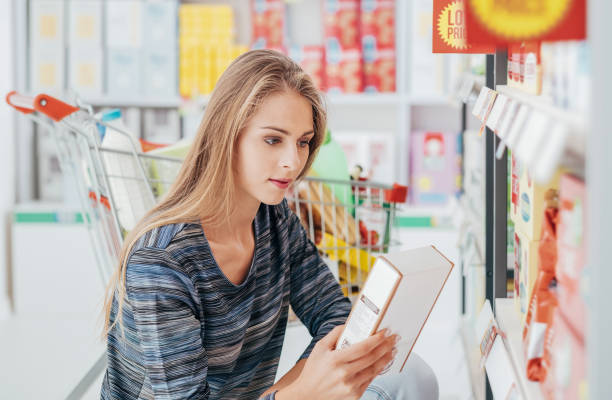 Woman reading food labels Young woman doing grocery shopping at the supermarket and reading a food label with ingredients on a box, shopping and nutrition concept labeling stock pictures, royalty-free photos & images