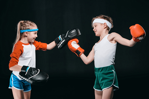 Side view of boy and girl in sportswear boxing isolated on black, activities for children concept
