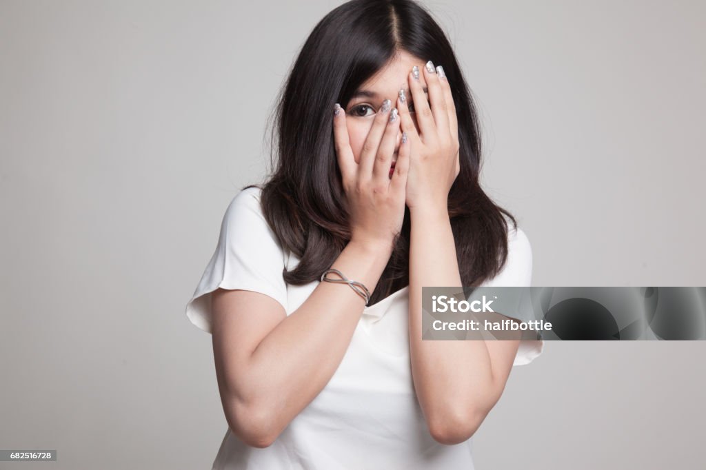 Beautiful young Asian woman peeking through fingers. Beautiful young Asian woman peeking through fingers on gray background 20-29 Years Stock Photo