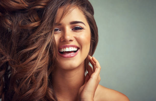 Lucious locks and happy laughter Studio portrait of a beautiful woman with long locks posing against a grey background human hair photos stock pictures, royalty-free photos & images