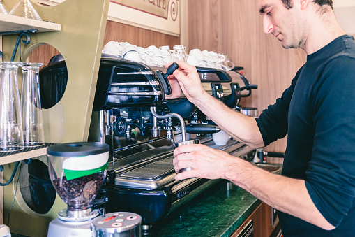 Coffee Shop interior: A bartender is using an espresso machine preparing coffee and heating milk to prepare a cappuccino