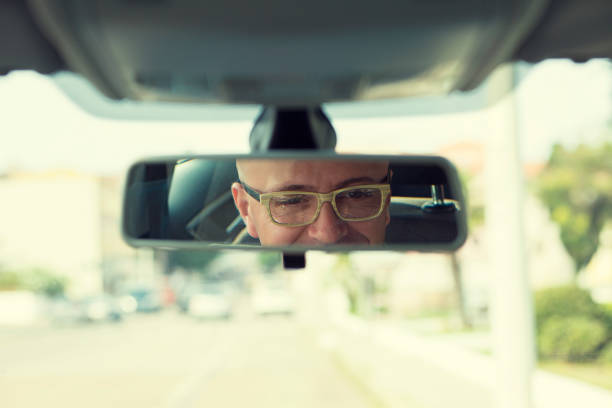 istock Closeup portrait, happy young man driver looking at rear view mirror smiling, isolated interior car windshield background. Positive human expression body language 682547552