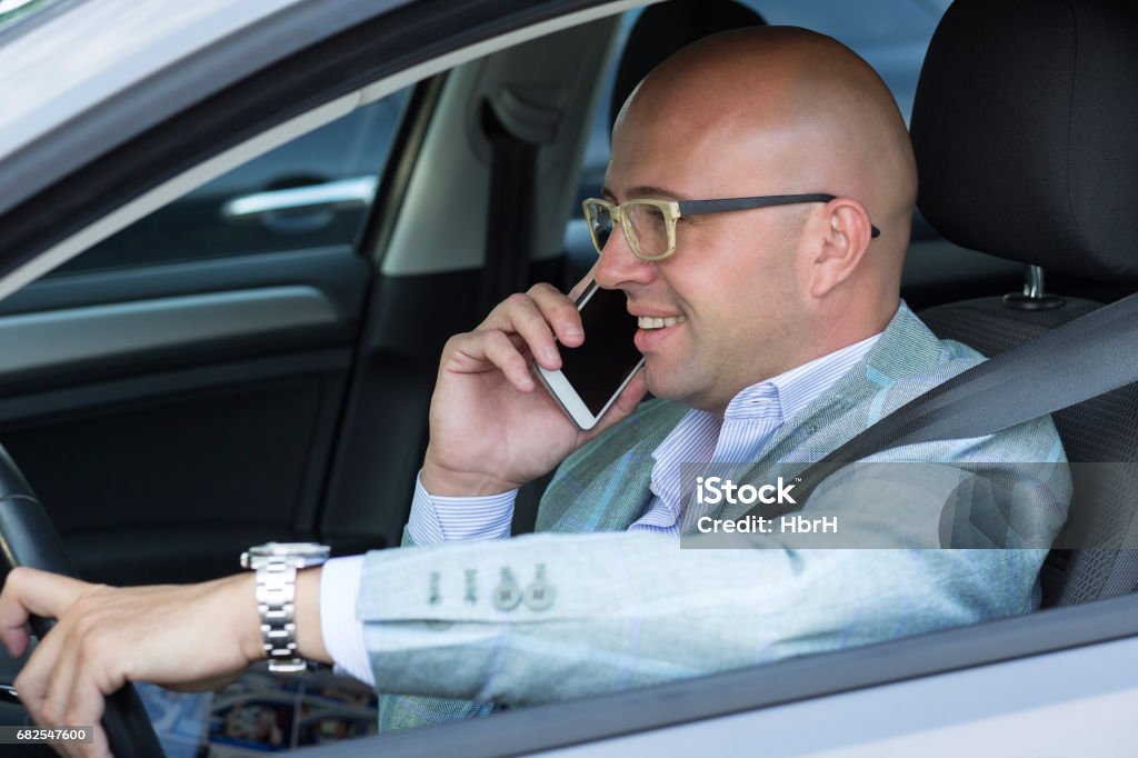 side view handsome successful young man smiling talking on mobile phone while driving his car . Risky, reckless driver bad habits. Traffic safety rule violation lack of attention concept Addiction Stock Photo