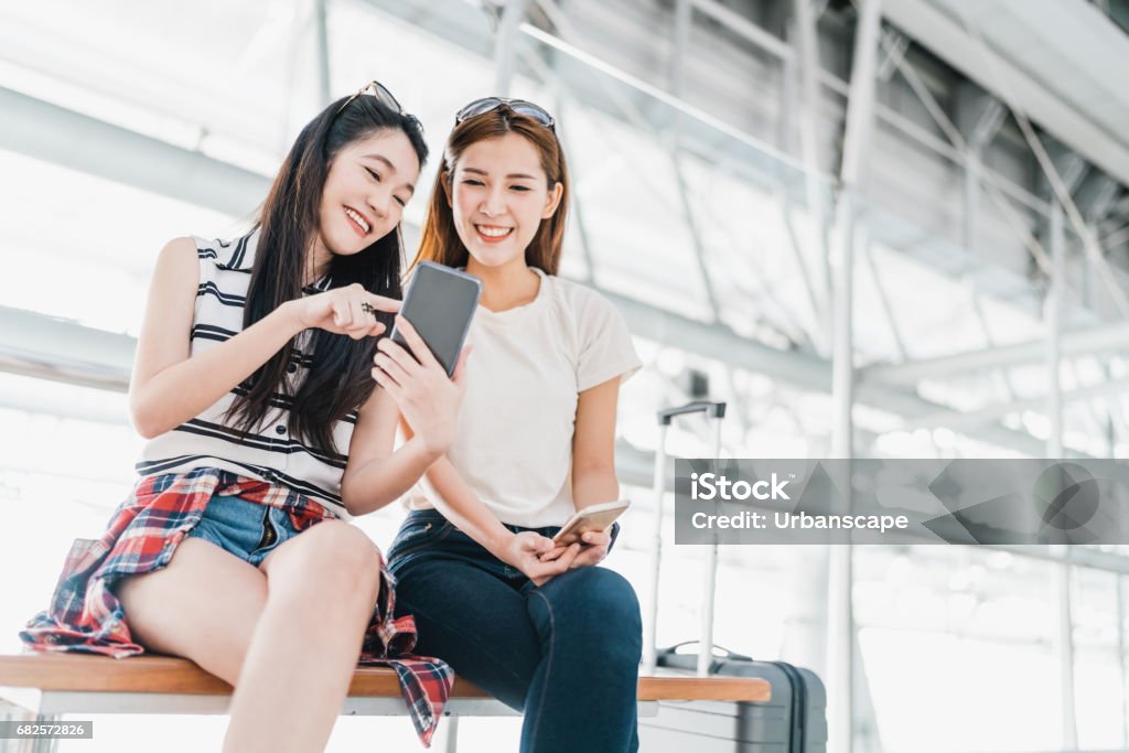 Zwei froh, dass asiatische Mädchen mit Smartphone überprüfen Flug oder online-Check-in am Flughafen zusammen mit dem Gepäck. Flugreisen, Sommerurlaub oder Handy-Anwendung-Technologie-Konzept - Lizenzfrei Reise Stock-Foto