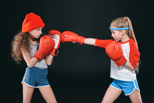 side view of sportive girls pretending boxing isolated on black, active kids concept