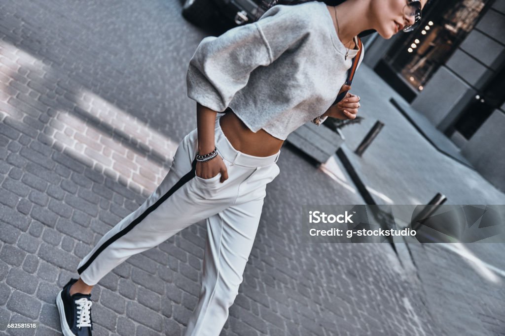 Confident in her fashion choices. Beautiful young woman keeping hand in pocket while walking outdoors Adult Stock Photo