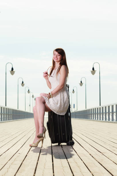 istock Woman sitting on suitcase, pier in background 682581712
