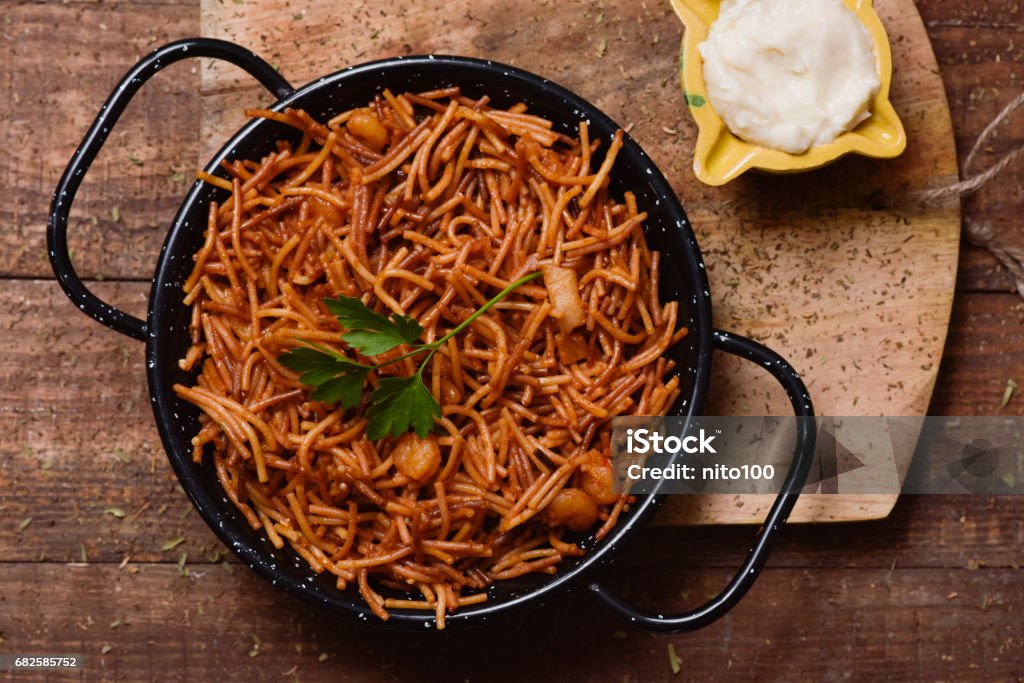 spanish fideua and aioli sauce high-angle shot of a spanish fideua, a typical noodles casserole with seafood, in a paella pan and aioli sauce in a yellow mortar on a rustic wooden table Fideuà Stock Photo