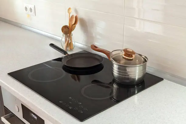 Photo of Open saucepan, pan and wooden spoons in modern kitchen with induction stove