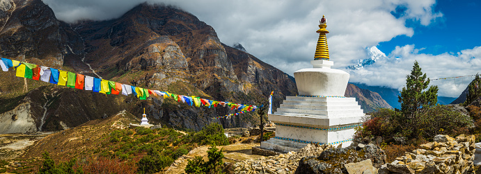 Brightly coloured Buddhist prayer flags fluttering in the thin mountain air beside traditional white washed stupas above the Sherpa village of Thame, high in the Sagarmatha National Park, Himalayas, Nepal.