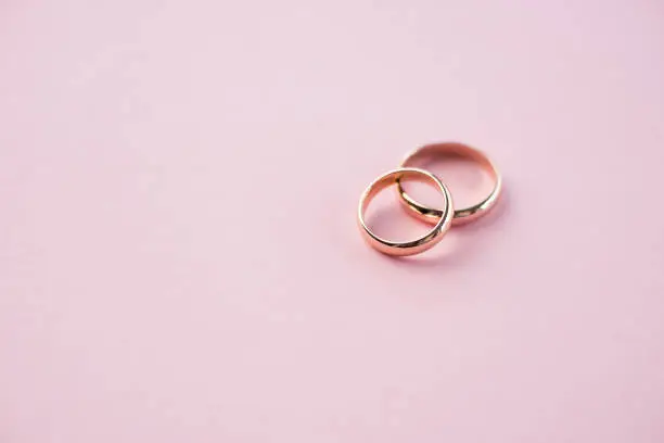 Photo of Close-up view of shiny golden wedding rings on pink, wedding rings background