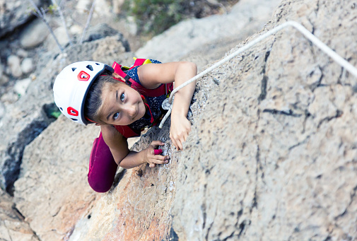 Portrait of little Baby Girl climbing vertical natural rock doing difficult move top view