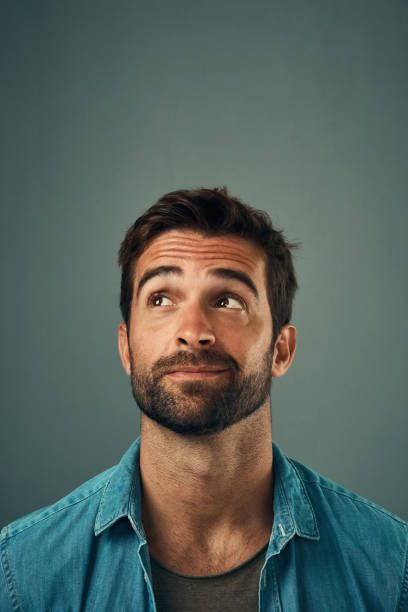 Something has caught his eye Studio shot of a handsome young man looking up against a grey background hair stubble stock pictures, royalty-free photos & images