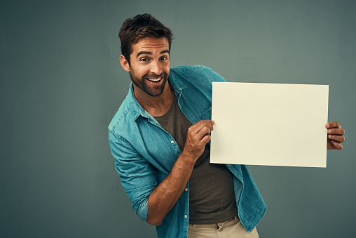 Studio portrait of a handsome young man holding a blank placard against a grey background