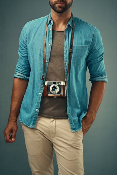 Studio shot of a young man posing with a vintage camera around his neck against a grey background