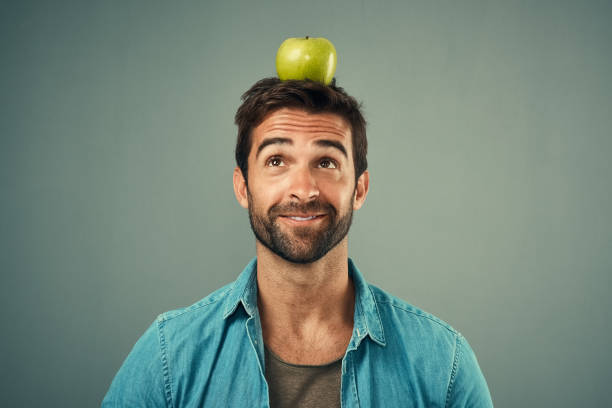 Studio shot of a handsome young man posing with an apple on his head against a grey background