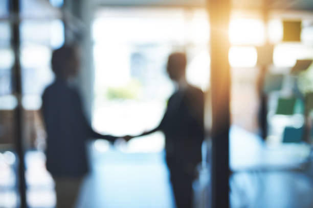 Let's call it a deal Defocused shot of two businesspeople shaking hands in an office merger stock pictures, royalty-free photos & images