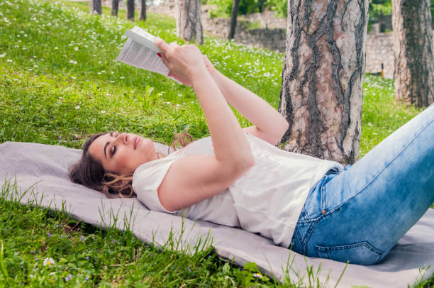 istock Young Woman reading book at park lying down on grass. 682632500