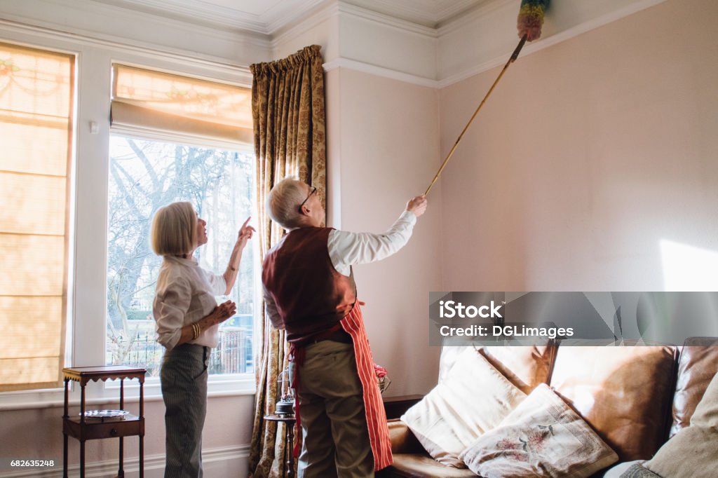 You've Missed A Spot! Senior man is helping his wife with the housework. He is using an extended feather duster to clean the ceiling and his wife is pointing out areas he has missed. Duster Stock Photo