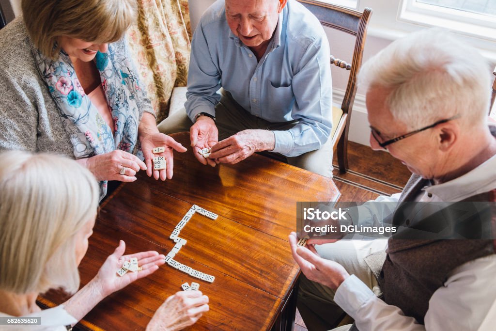 Seniors Playing Dominoes Group of senior friends are playing dominoes at a table together. Senior Adult Stock Photo