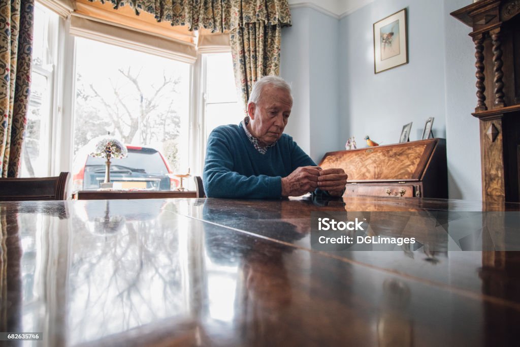 Worried Old Man Senior man is sitting alone at the dining table in his home, with a worried expression on his face. Senior Adult Stock Photo