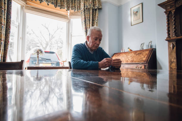 Worried Old Man Senior man is sitting alone at the dining table in his home, with a worried expression on his face. old man depressed stock pictures, royalty-free photos & images