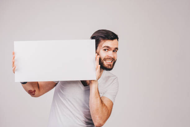 istock unshaved man in white t-shirt holding a blank white board 682640264