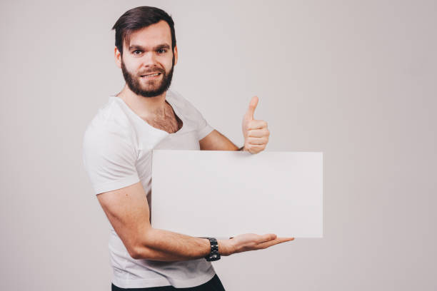 istock unshaved man in white t-shirt holding a blank white board 682640348