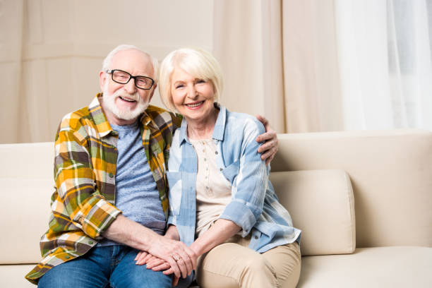 istock Happy senior couple sitting embracing on sofa and smiling at camera 682658560