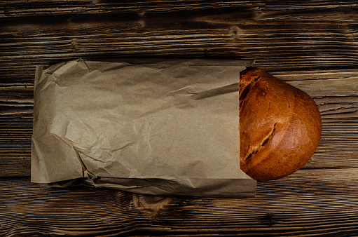 Loaf of bread in a paper bag on wooden table. Top view