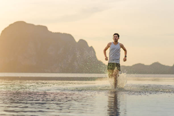 istock Young asian man running on beach with sunset in background 682676424