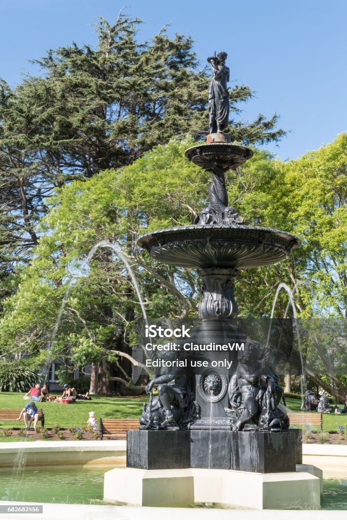 Closeup of Victorian fountain in Albart Park, Auckland. Auckland, New Zealand - March 5, 2017: Closeup of Black metal 19th century Victorian Fountain in center of Albert Park. Green vegetation, people in back under blue sky. Albert Park Stock Photo