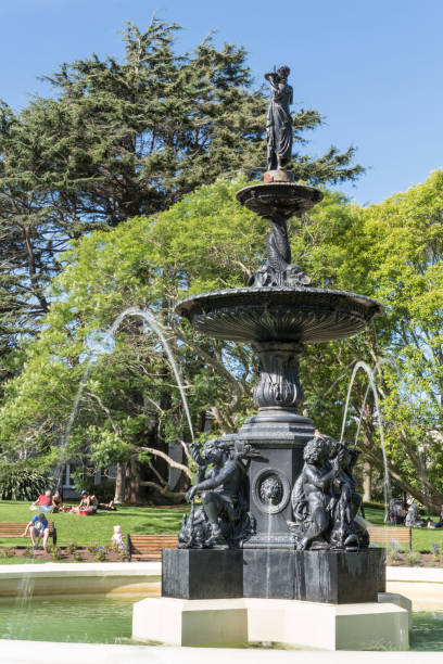 Closeup of Victorian fountain in Albart Park, Auckland. Auckland, New Zealand - March 5, 2017: Closeup of Black metal 19th century Victorian Fountain in center of Albert Park. Green vegetation, people in back under blue sky. albert park stock pictures, royalty-free photos & images