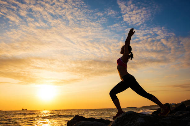 istock Young woman silhouette practicing yoga on the sea beach at sunset 682682778