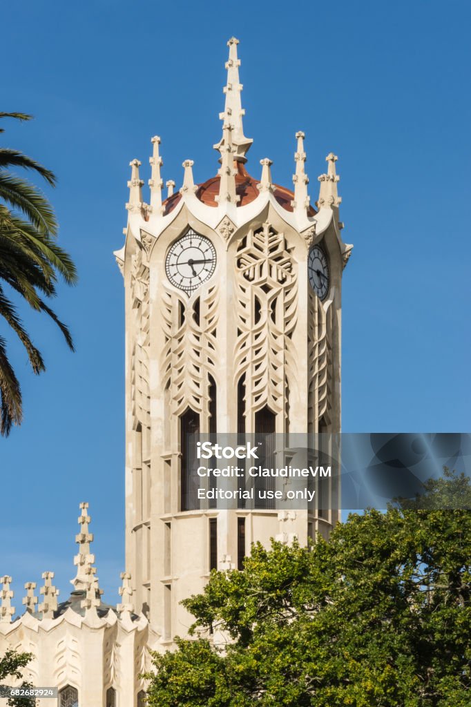 Closeup of Clock tower top of Auckland University. Auckland, New Zealand - March 5, 2017: Closeup of White clock tower top of Auckland University under blue sky. Some green tree leaves. Auckland Stock Photo