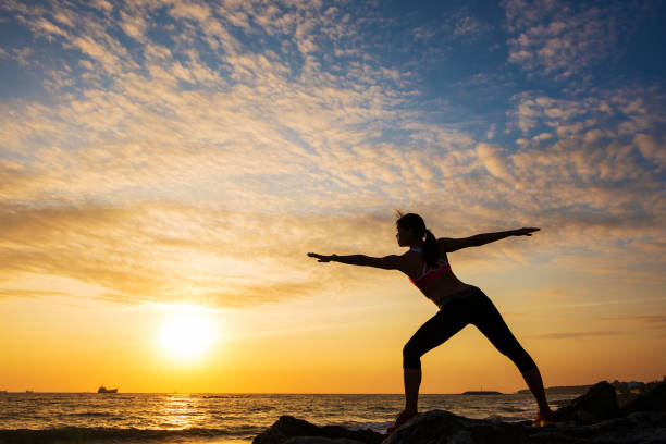 istock Young woman silhouette practicing yoga on the sea beach at sunset 682682998