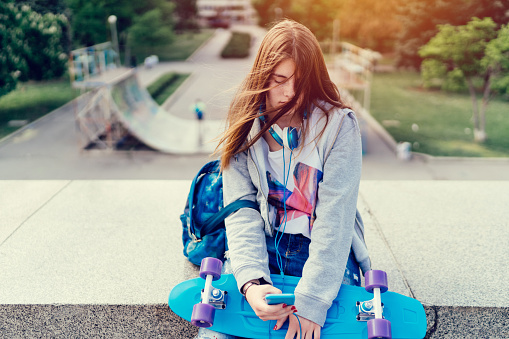 Depressed teenage girl in the city park using smartphone