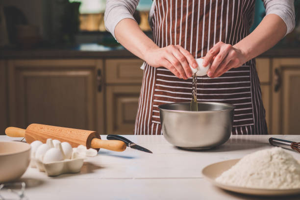 istock Young woman breaking egg over bowl with dough, close-up 682690072